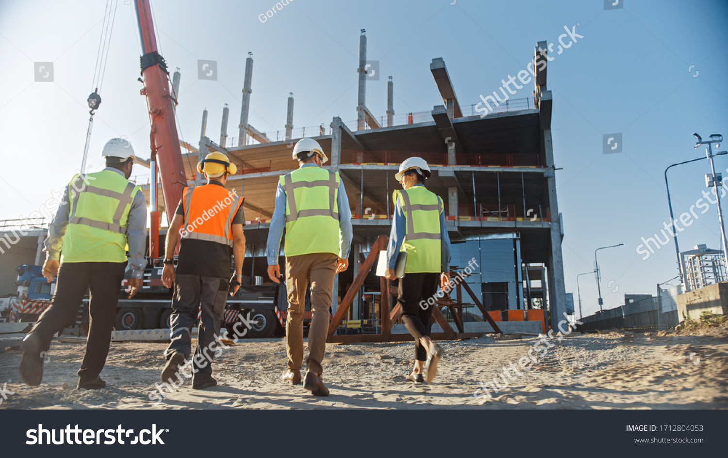 Diverse Team of Specialists Inspect Commercial, Industrial Building Construction Site. Real Estate Project with Civil Engineer, Investor and Businesswoman. In the Background Skyscraper Formwork Frames #1712804053