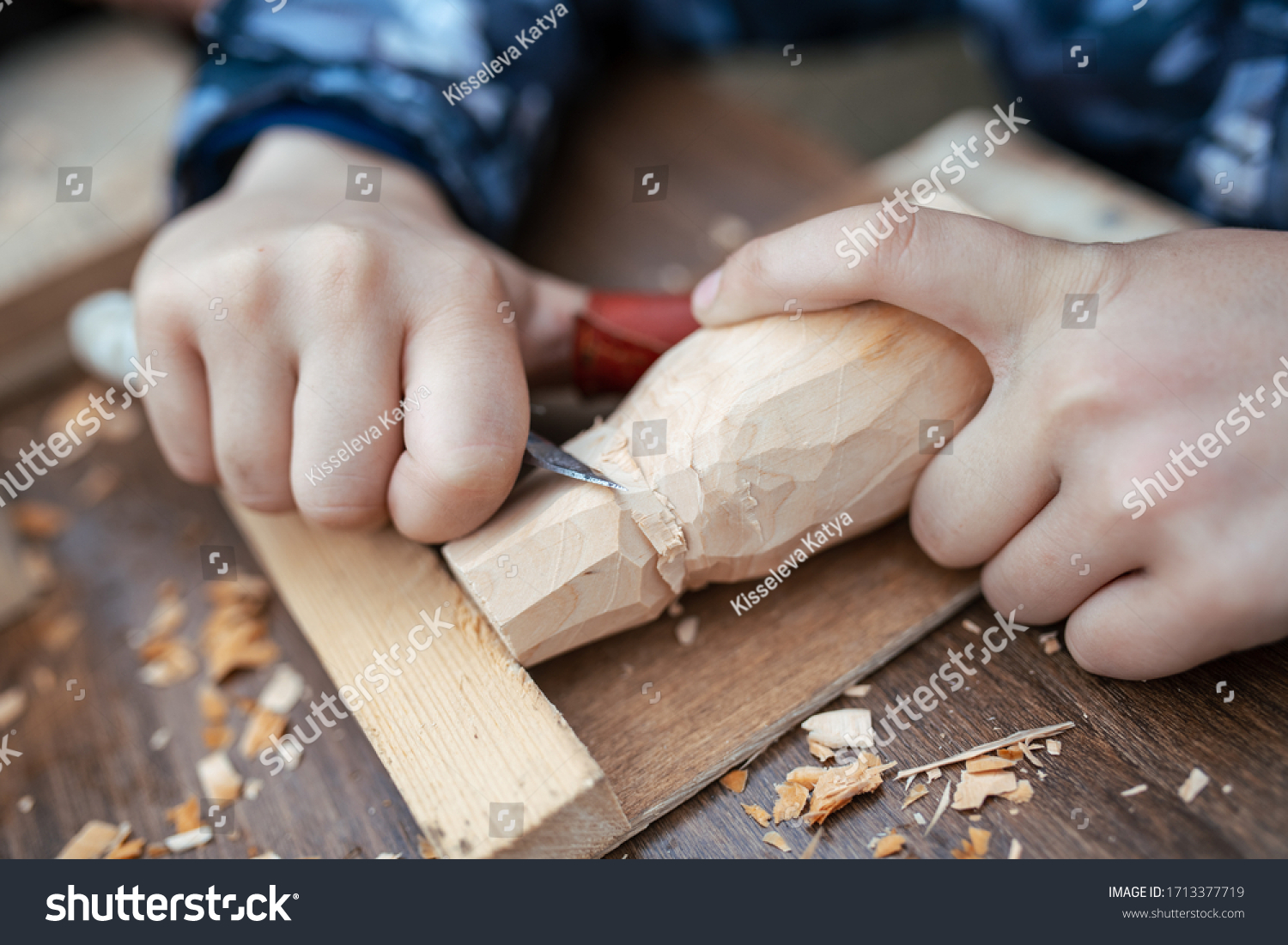 child carves a toy in wood with a knife.  carpenter in the workshop. Close-up of hands  #1713377719