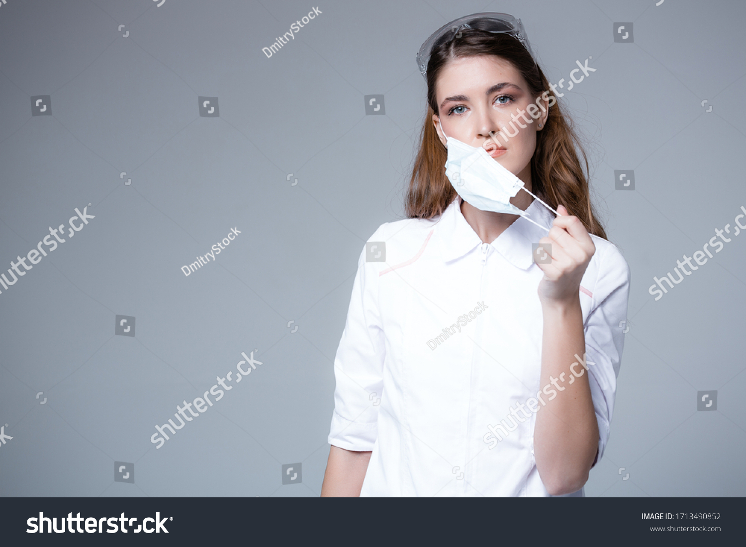 A young doctor takes off a disposable medical mask. Lack of masks and the risk of getting sick without face protection #1713490852