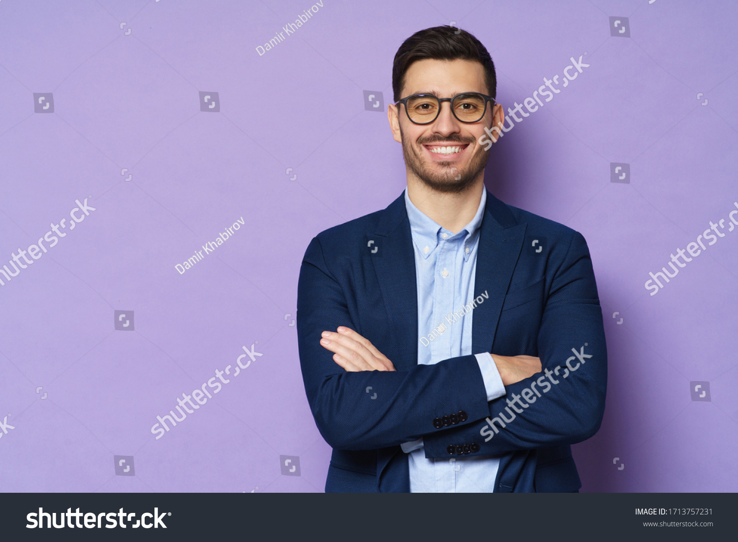 Young buisnessman wearing eyeglasses, jacket and shirt, holding arms crossed, looking at camera with happy confident smile, standing against purple background #1713757231