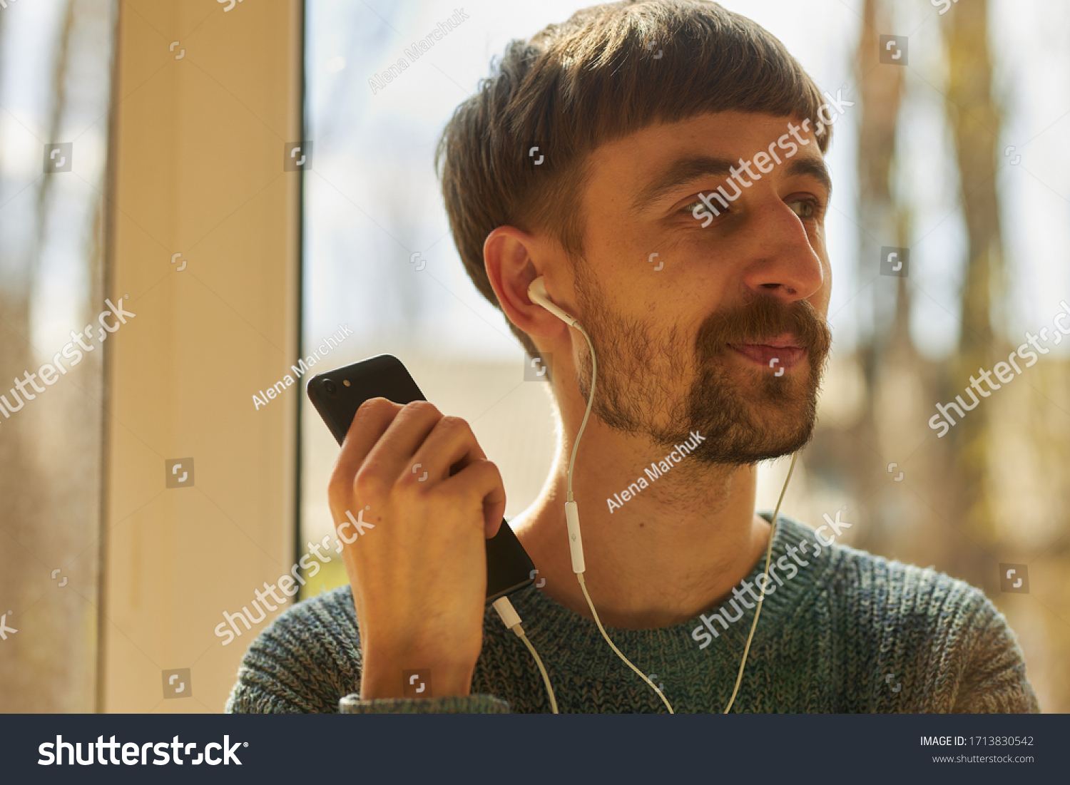 A bearded man is listening to music on headphones. The guy listens to music on headphones and enjoys. #1713830542