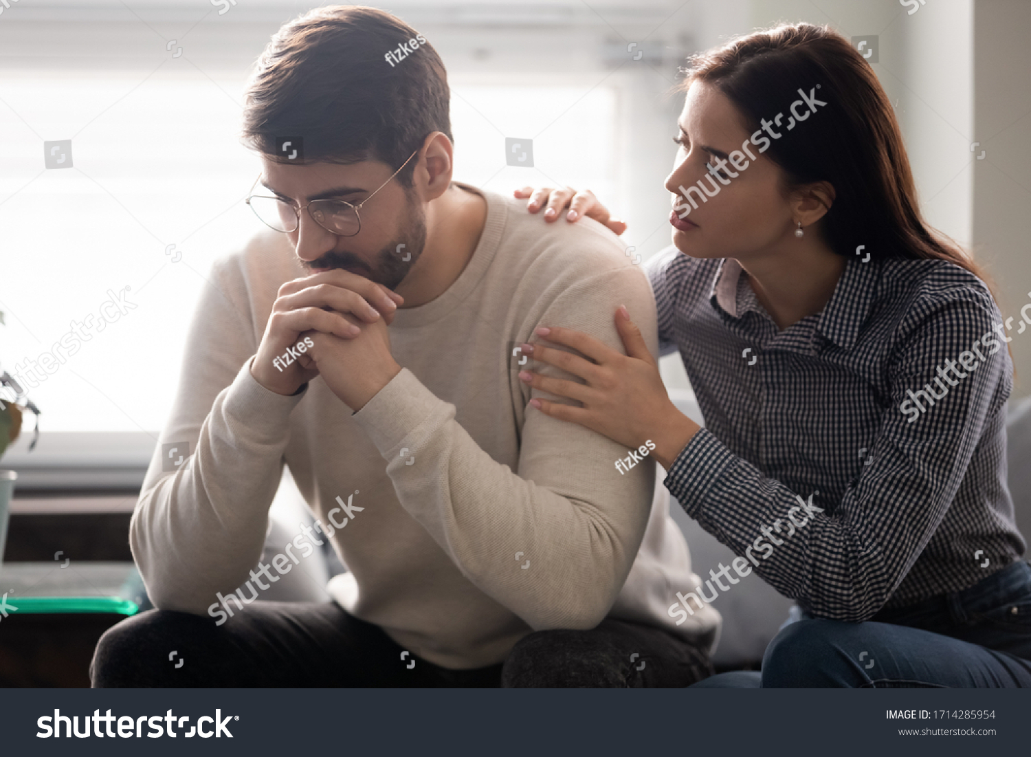 Attractive wife comforting husband embrace and showing support. Woman upset man, expressing sympathy and understanding, say sorry, family sitting on comfortable sofa at home. #1714285954