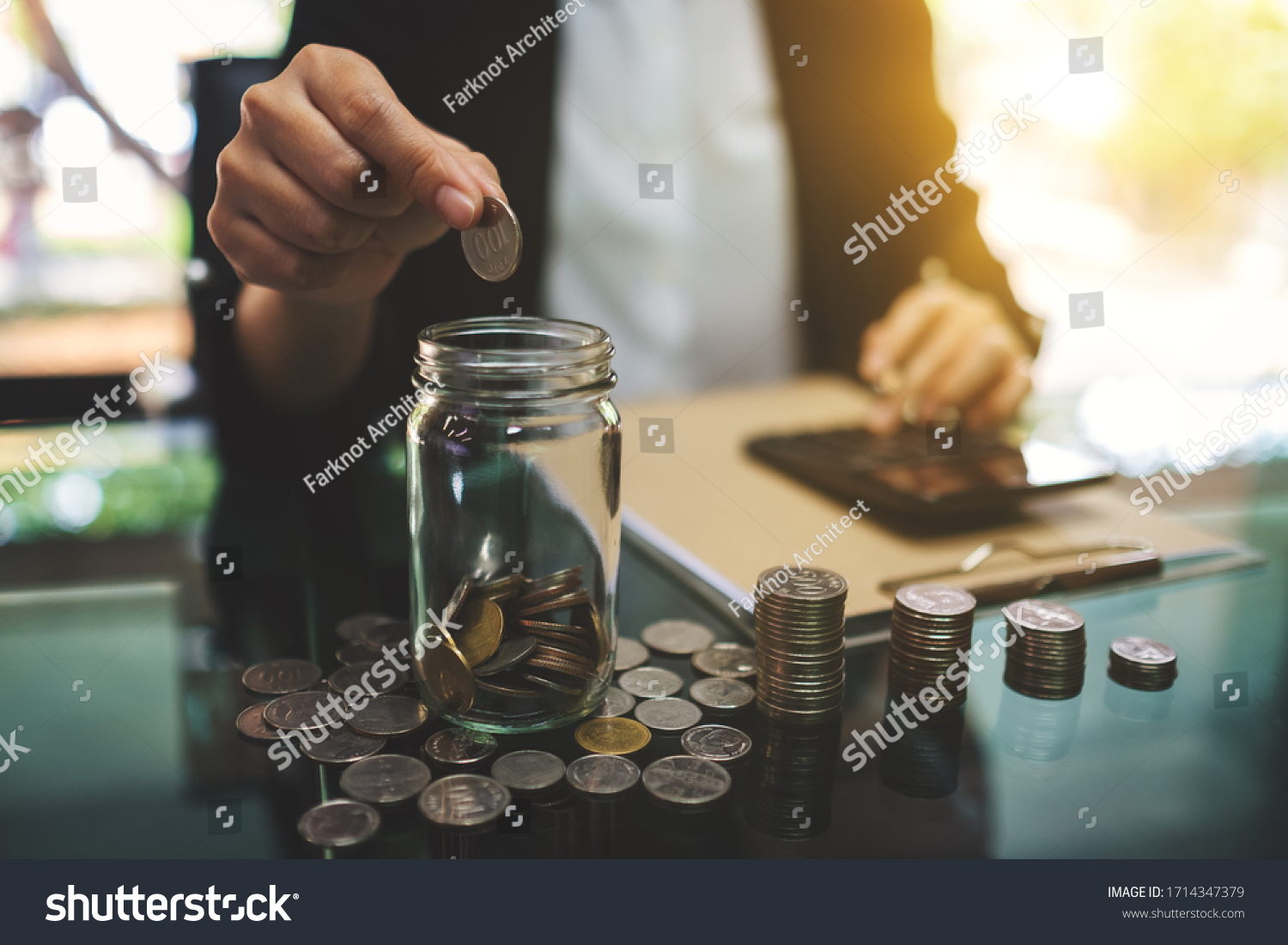 Closeup image of a businesswoman calculating, stacking and putting coins in a glass jar for saving money and financial concept #1714347379