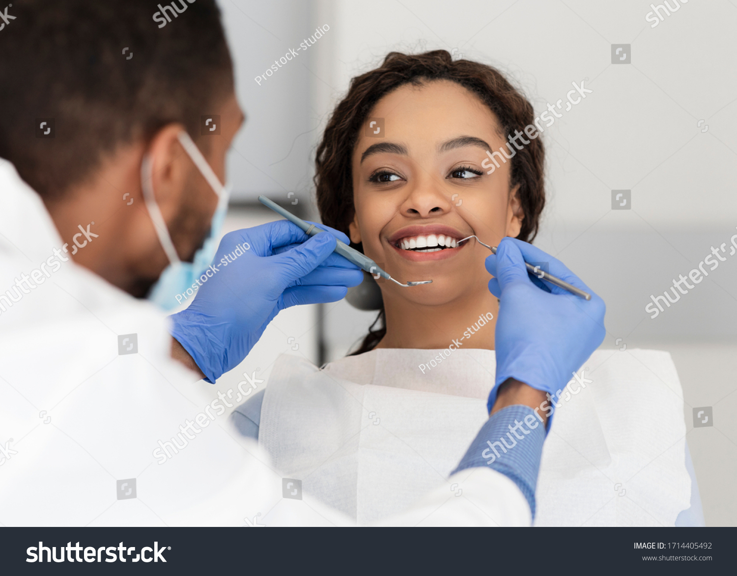 Pretty black lady in dentist chair looking at her doctor with smile, close up #1714405492