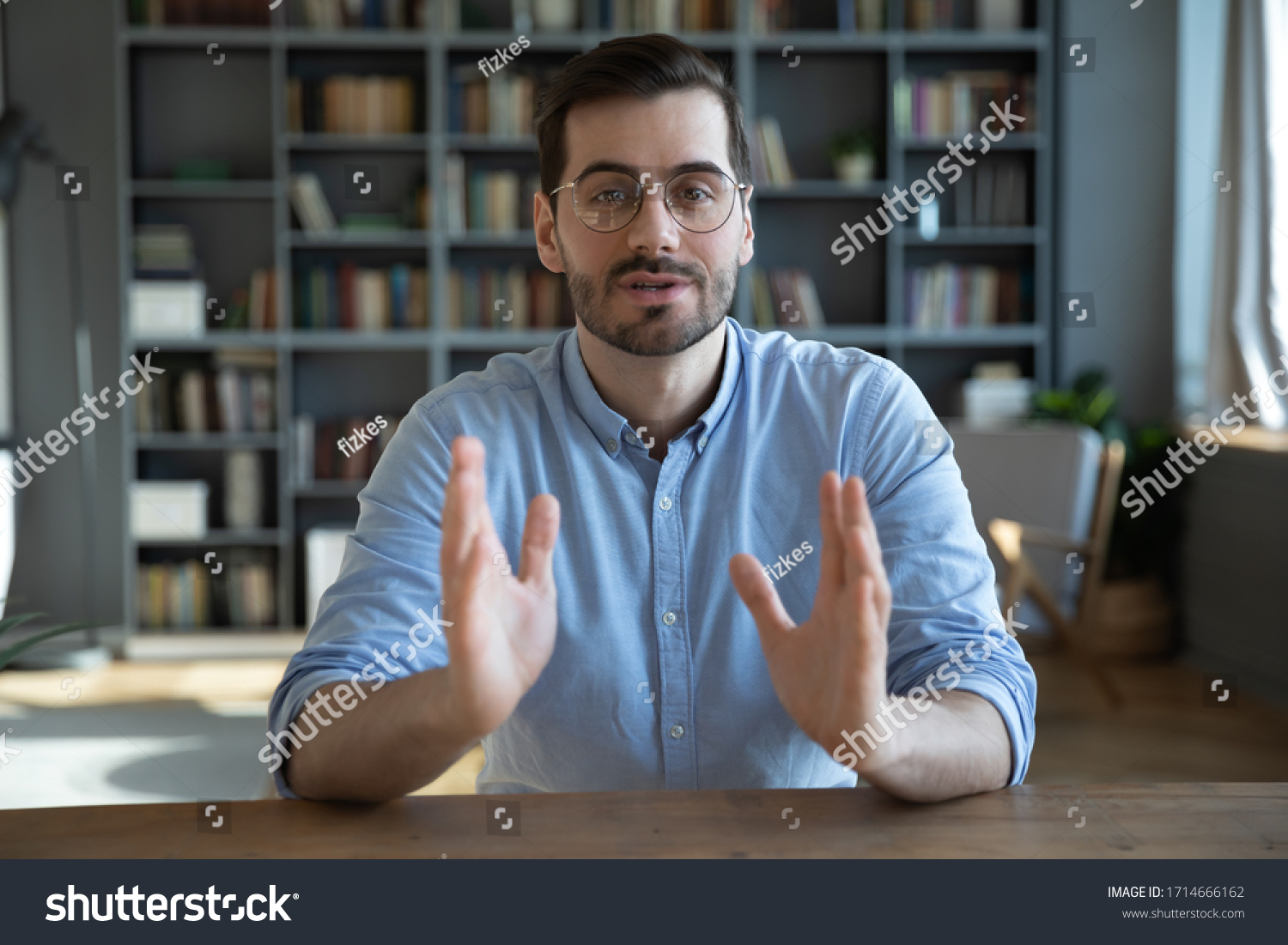 Head shot portrait confident businessman coach wearing glasses looking at camera and talking, mentor speaker holding online lesson, explaining, sitting at wooden work desk in modern cabinet #1714666162