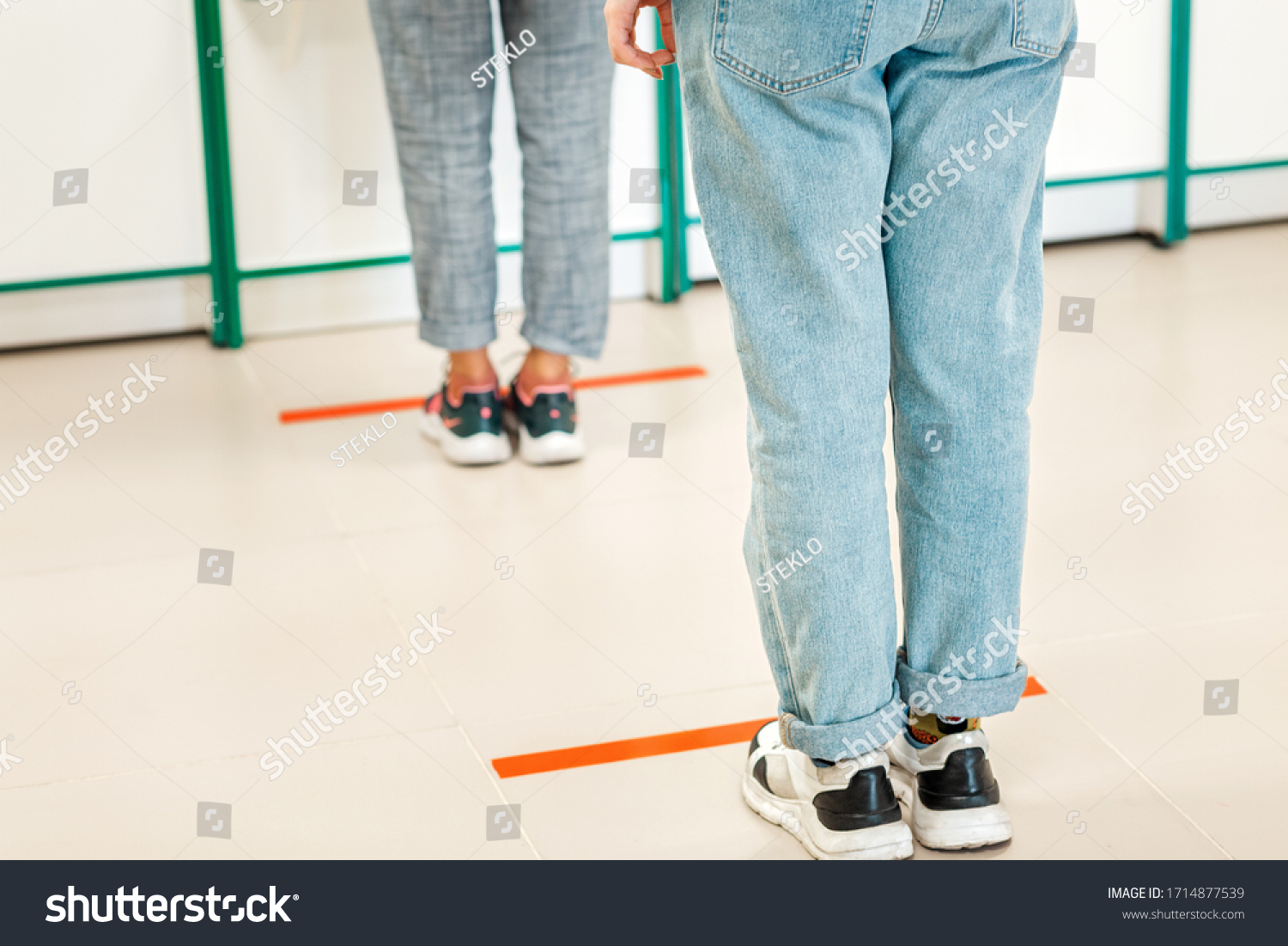 People stand in line, legs close-up. Attention line on the floor of the store to maintain social distance. Concept of the coronavirus pandemic and prevention measures #1714877539