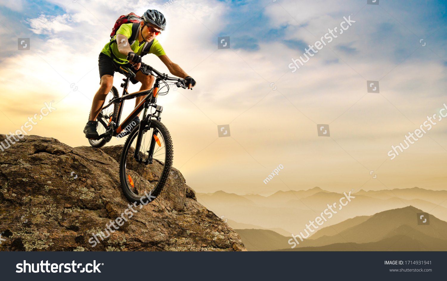 Cyclist Riding the Bike Down the Rock at Sunrise in the Beautiful Mountains on the Background. Extreme Sport and Enduro Biking Concept. #1714931941