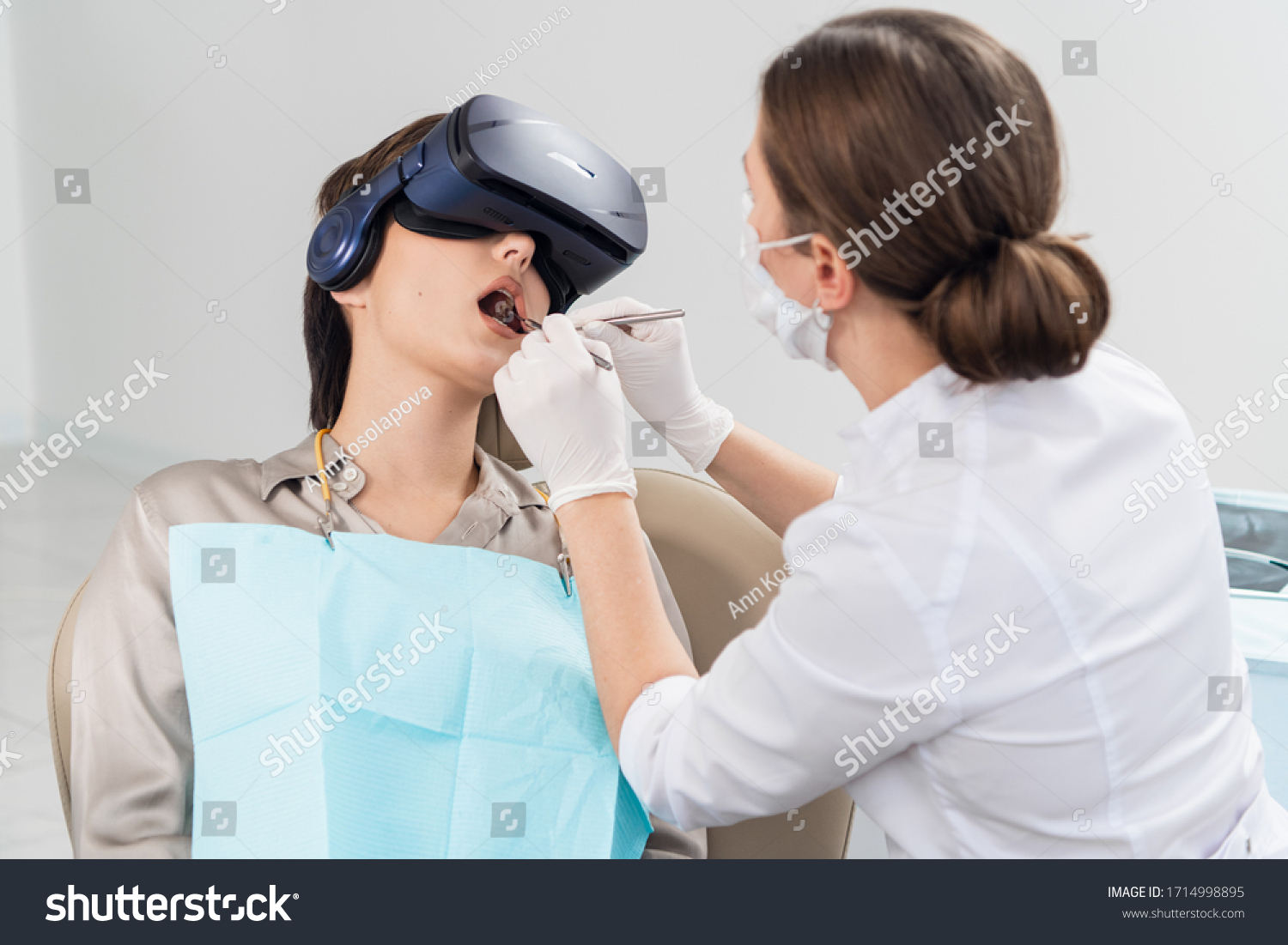 The dentist is doing her job, while the patient is lying with her mouth wide open, wearing VR glasses #1714998895