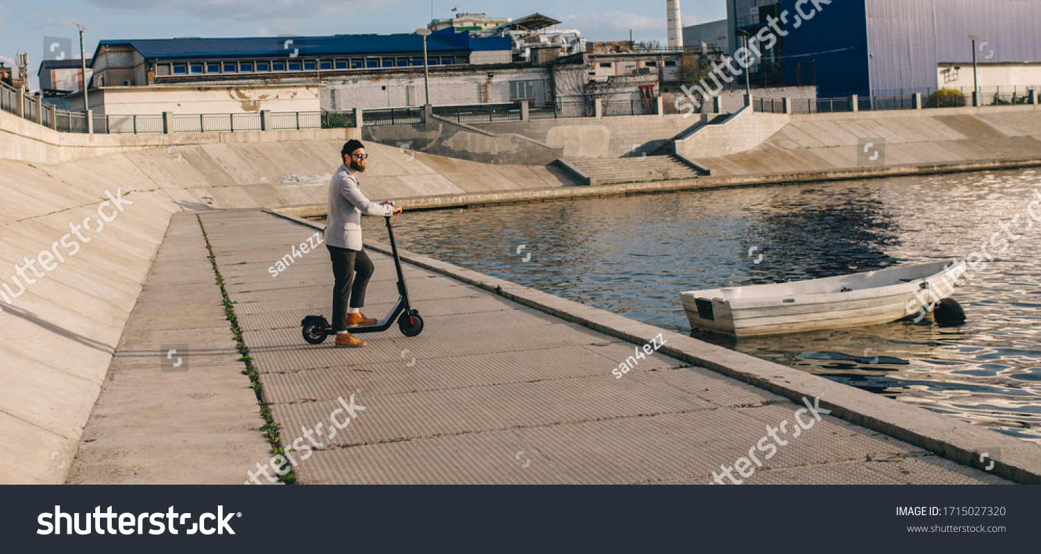 Young hipster man in a suit riding an electric scooter in bright sunny day. Ecological transportation concept. #1715027320