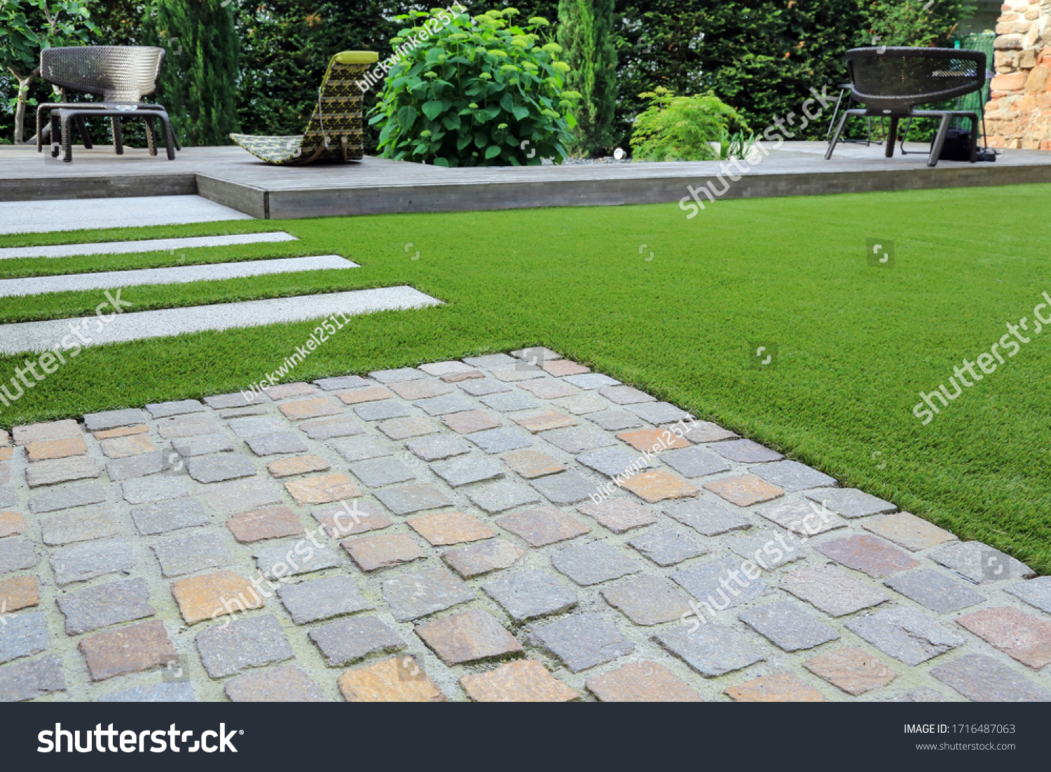 Modern garden design and terrace construction with a material mix of cobble paving stones and concrete paving slab and artificial lawn and wood #1716487063