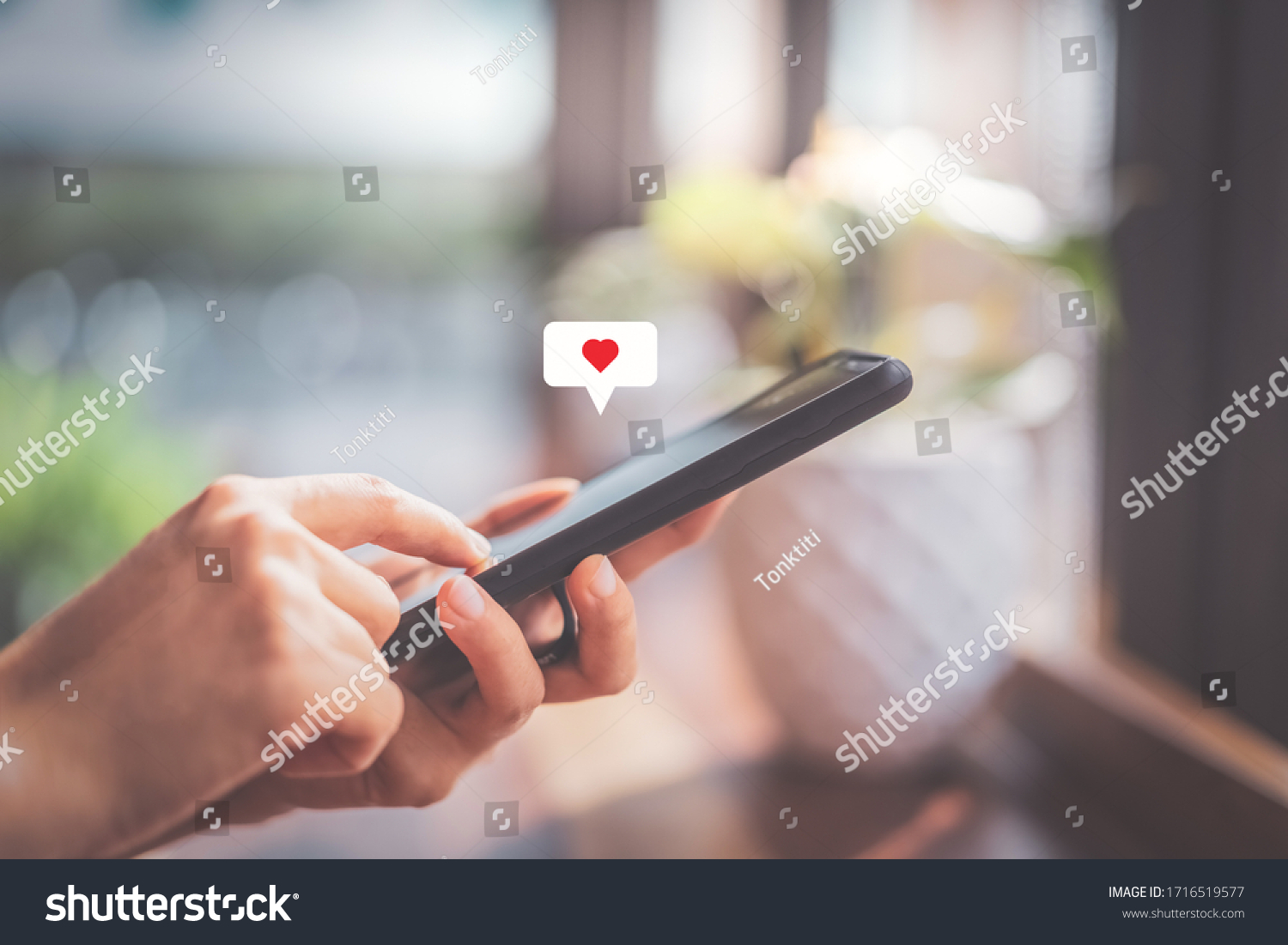Woman hand using smartphone with heart icon at coffee shop background. Technology business and social lifestyle concept. Vintage tone filter effect color style. #1716519577