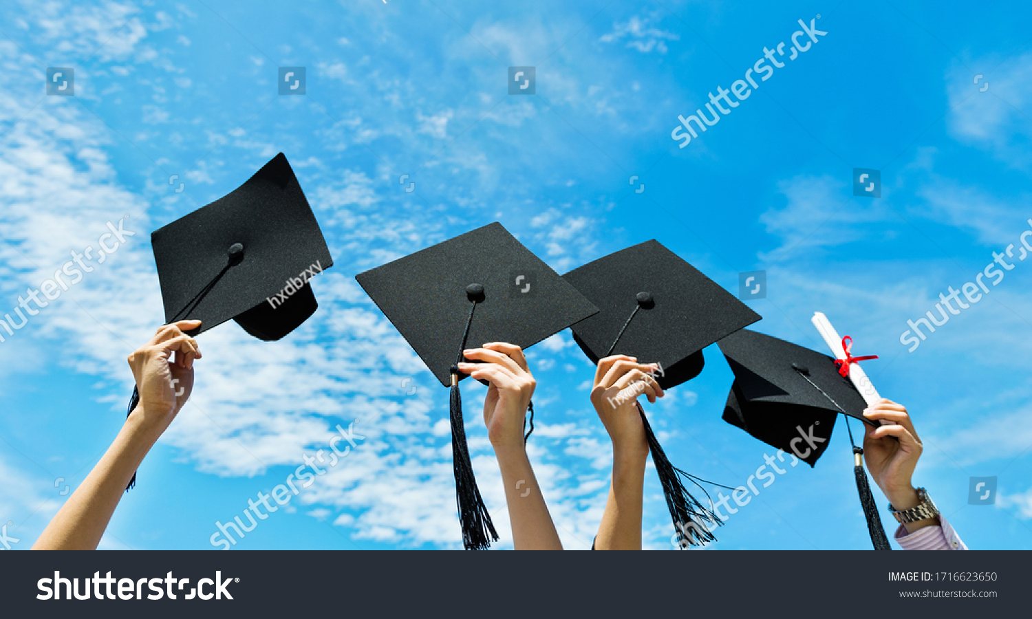 Four hands holding graduation hats on background of blue sky. #1716623650