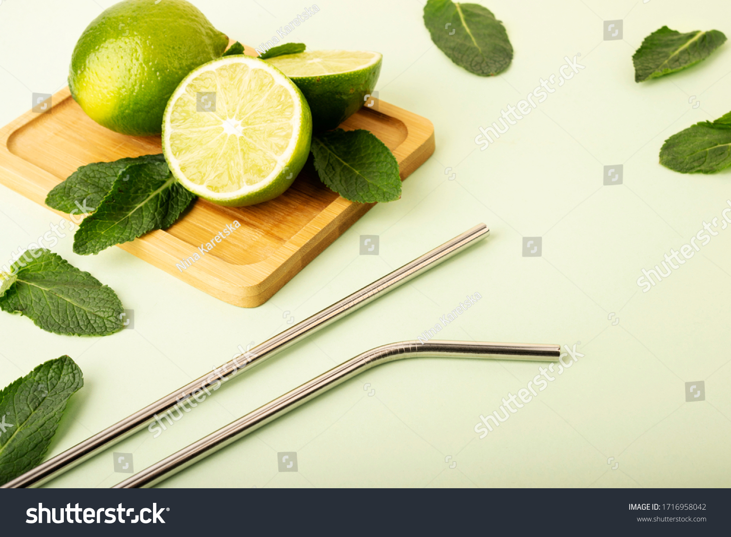 Reusable metal straws on a pastel background. Fresh lime and mint fruits lie on a wooden stand. Green color and fruts emphasize. Reusable environmental products, zero waste.Eco products #1716958042