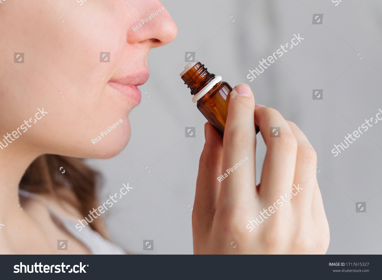 Aromatherapy: a girl with beautiful skin holds a bottle of essential oil near her nose and inhales. Close up, bright marble background. #1717615327