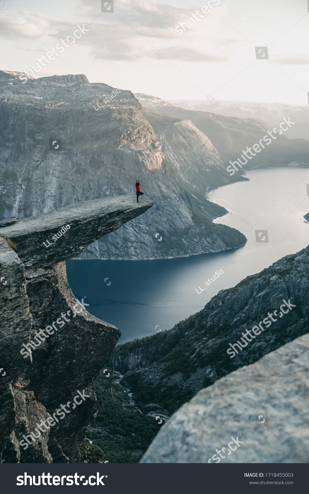 Woman standing in yoga pose on rock on troll tongue in Norway at sunset. Eka Pada Pranamasana #1718455003