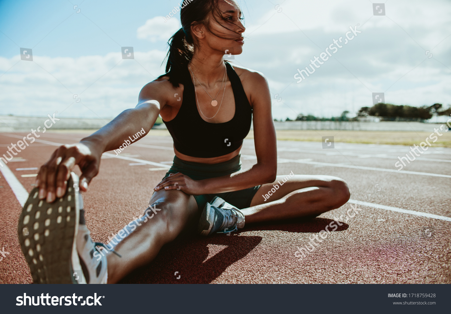 Athlete doing stretching exercises on running track. Woman runner stretching leg muscles by touching his shoes and looking away. #1718759428