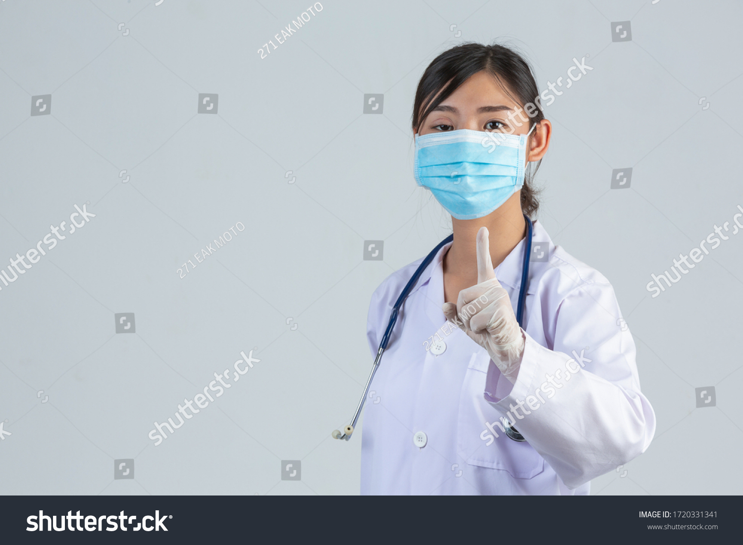 Beautiful young doctor is wearing mask while raised her index finger on white background. #1720331341