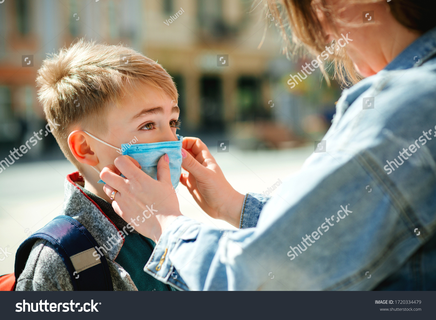 Mother puts a safety mask on her son's face. Schoolboy is ready go to school. Cute boy with a backpack outdoors. Back to school concept. Medical mask to prevent coronavirus. Coronavirus quarantine #1720334479