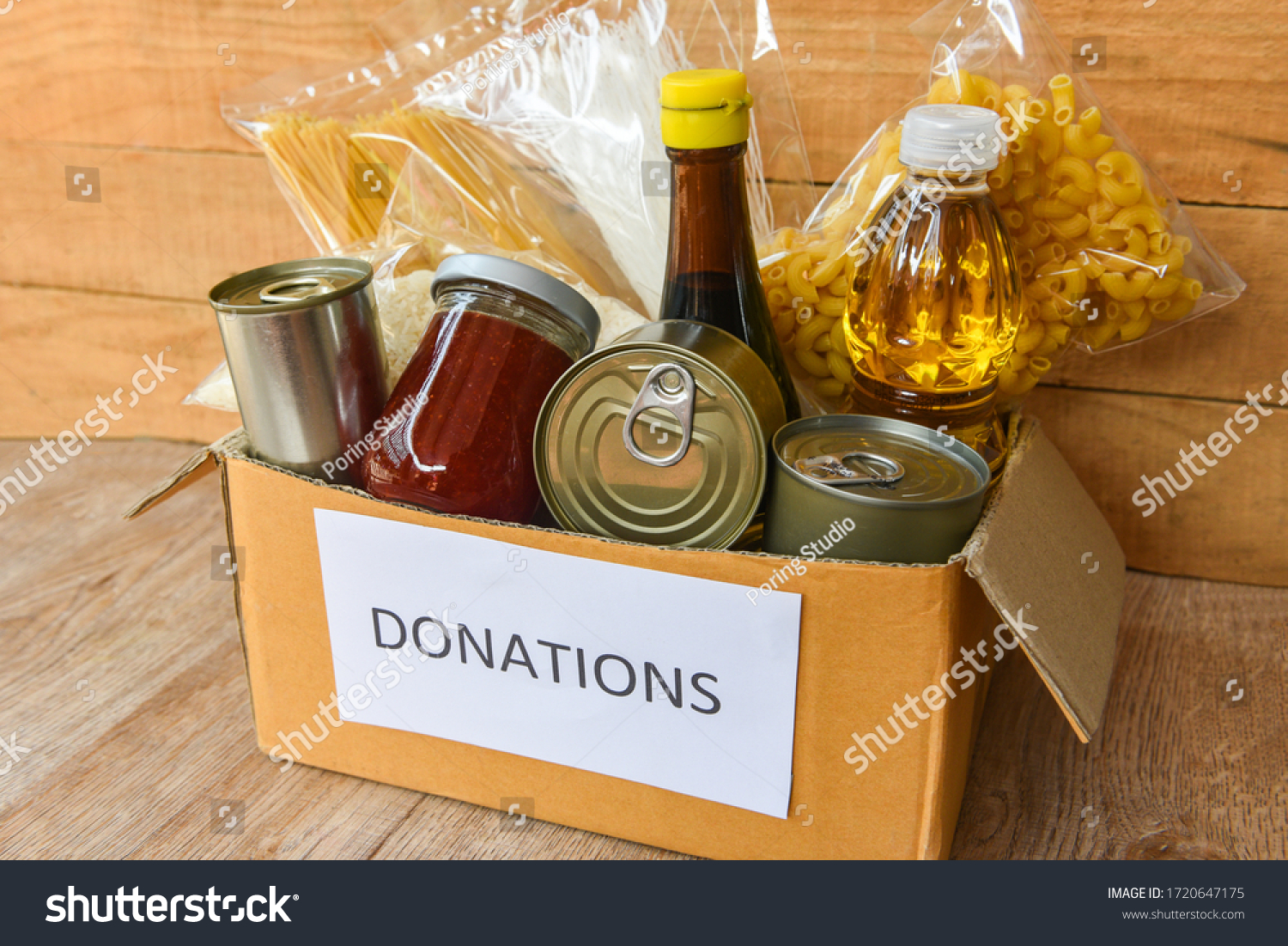 Donations box with canned food on wooden table background / pasta canned goods and dry food non perishable with cooking oil rice noodles spaghetti macaroni donations food concept #1720647175