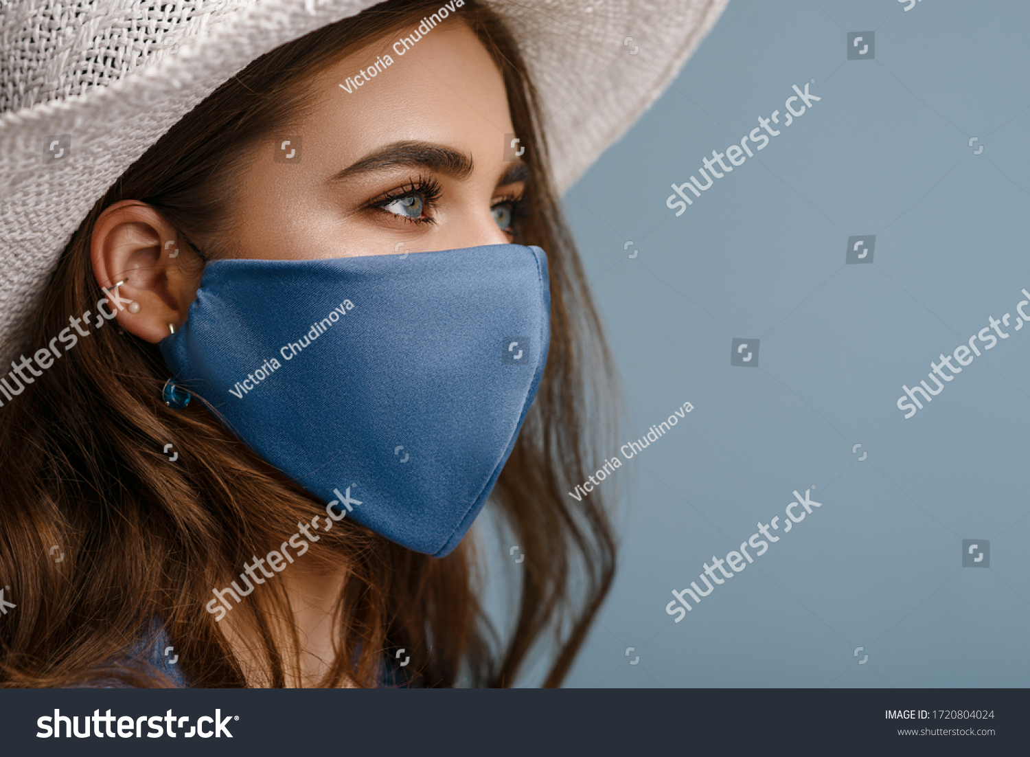 Woman wearing stylish protective face mask, posing on blue background. Trendy Fashion accessory during quarantine of coronavirus pandemic. Close up studio portrait. Copy, empty space for text #1720804024