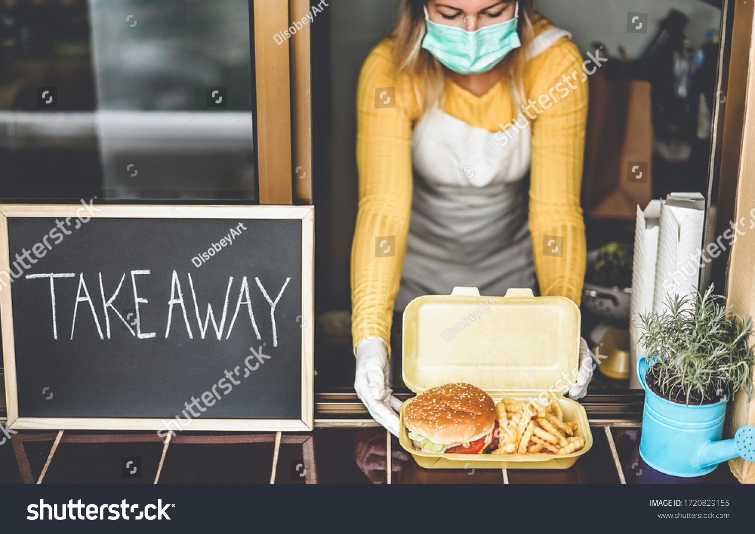 Young woman preparing takeaway food inside restaurant during Coronavirus outbreak time - Worker inside kitchen cooking fast food for online order service - Focus on hamburger #1720829155