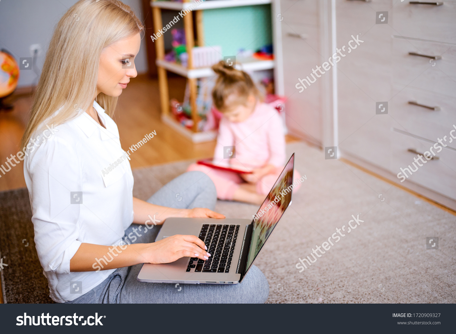 Young happy mother works on a computer at home on the floor, the child watches multifilny on a digital tablet, plays games on the computer, family concept. #1720909327