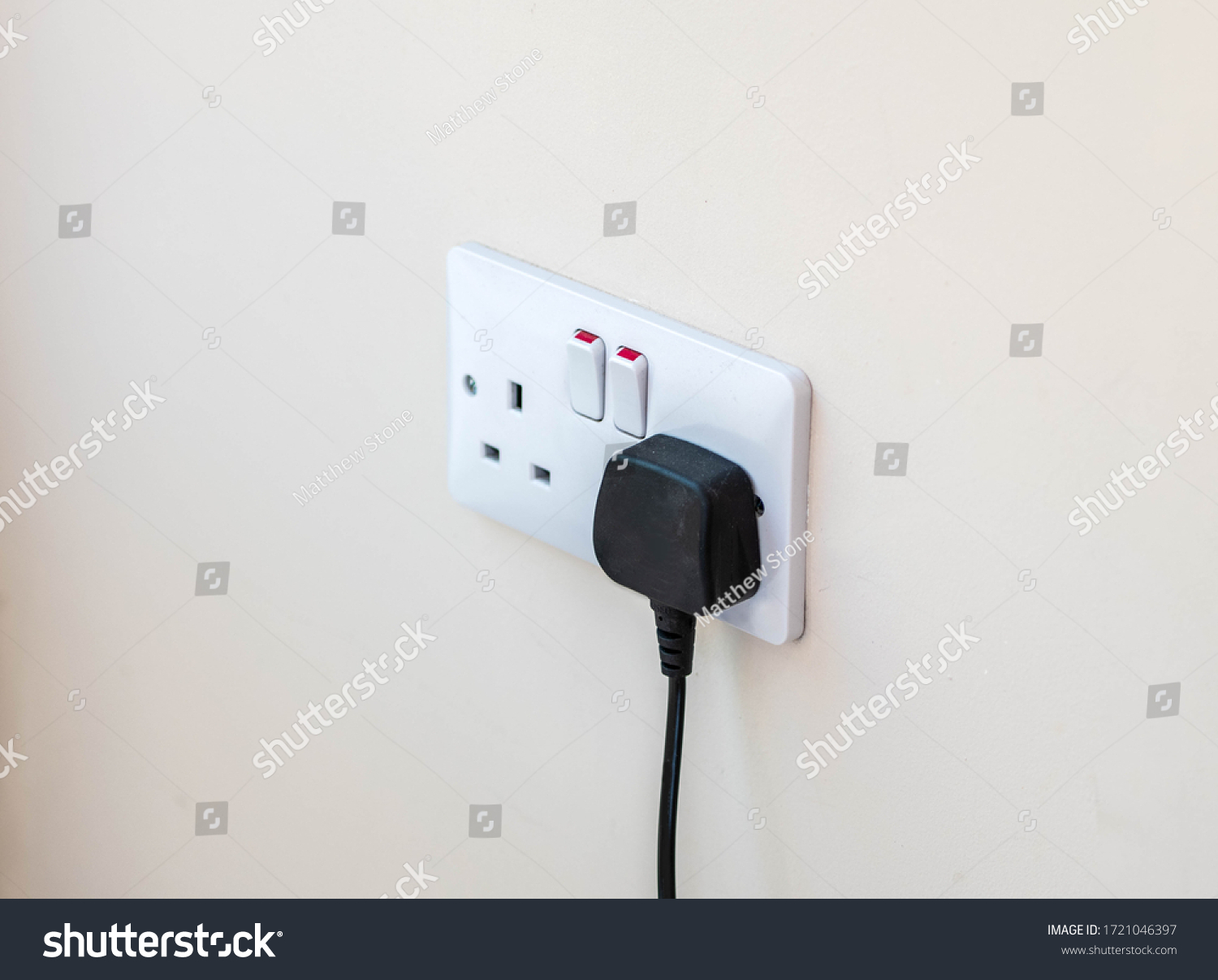Uk plug socket with a black plug plugged in wasting electricity  #1721046397
