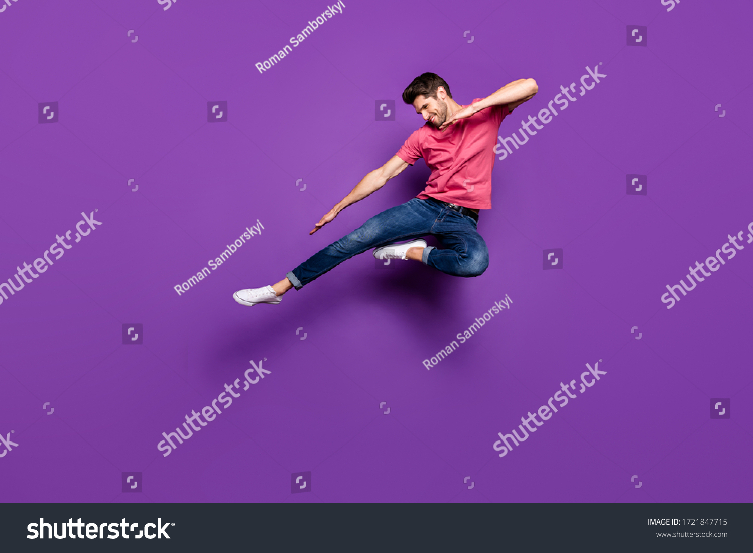 Full length photo of handsome attractive guy jump high up spread arms dance strange dab moves wear casual pink t-shirt jeans footwear isolated purple color background #1721847715