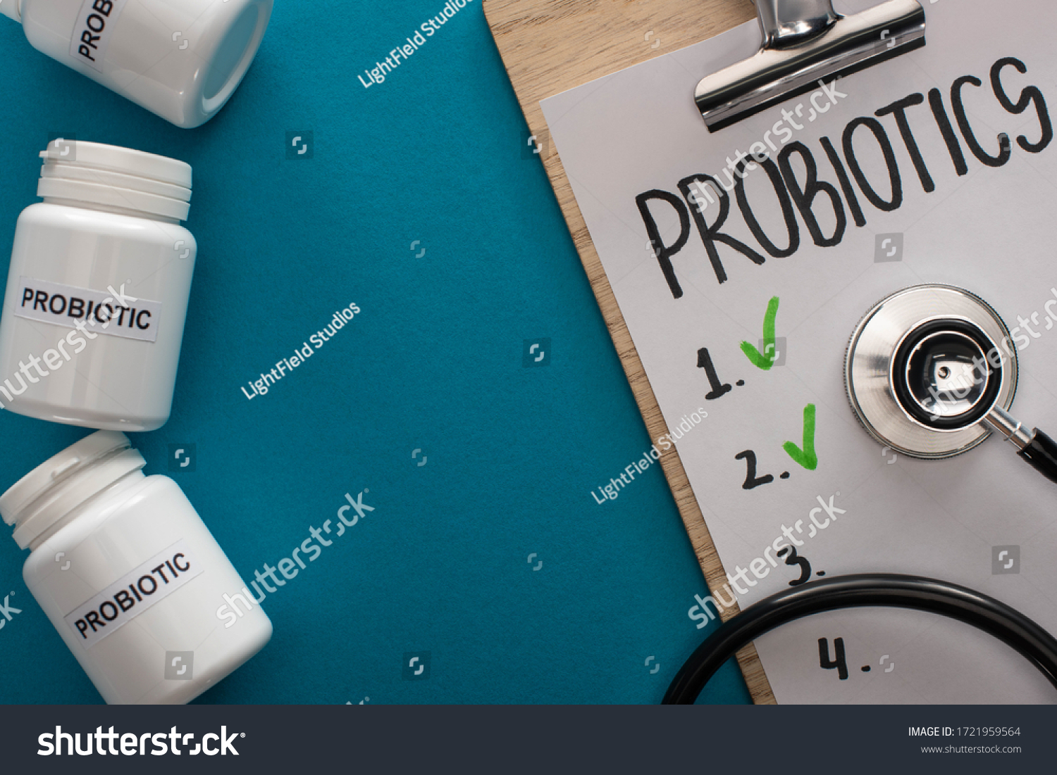 top view of clipboard with probiotics empty list with stethoscope near containers with pills on blue background #1721959564