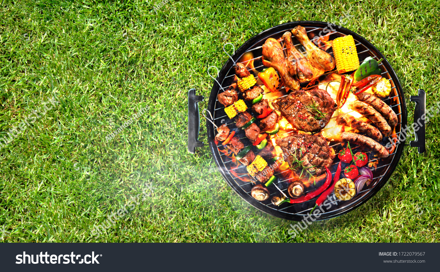 Top view of assorted delicious grilled meat with vegetables on barbecue grill with smoke and flames in green grass #1722079567