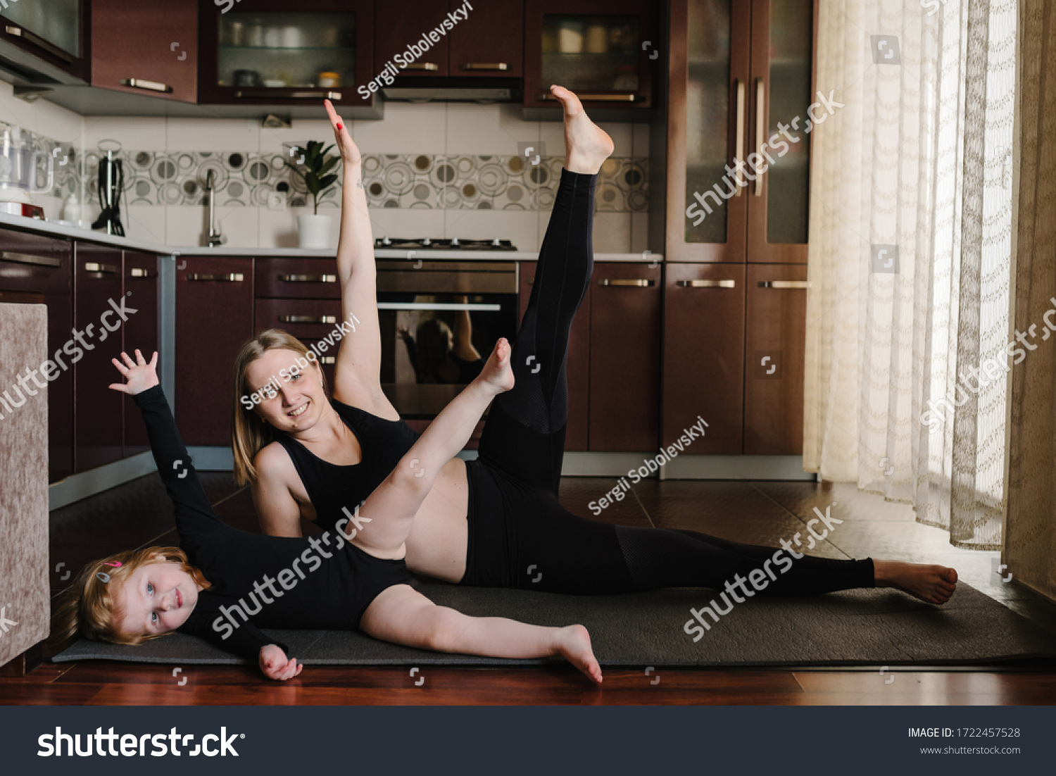 Mother and daughter are training at home. Happy family playing sports in the kitchen. Mom and kid are practicing yoga. Sports mom with child doing morning work-out, do the exercises together, healthy. #1722457528