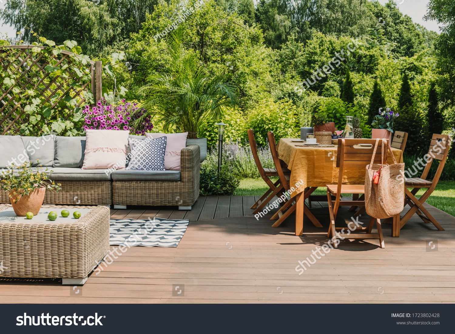 Dining table covered with orange tablecloth standing on wooden terrace in green garden #1723802428