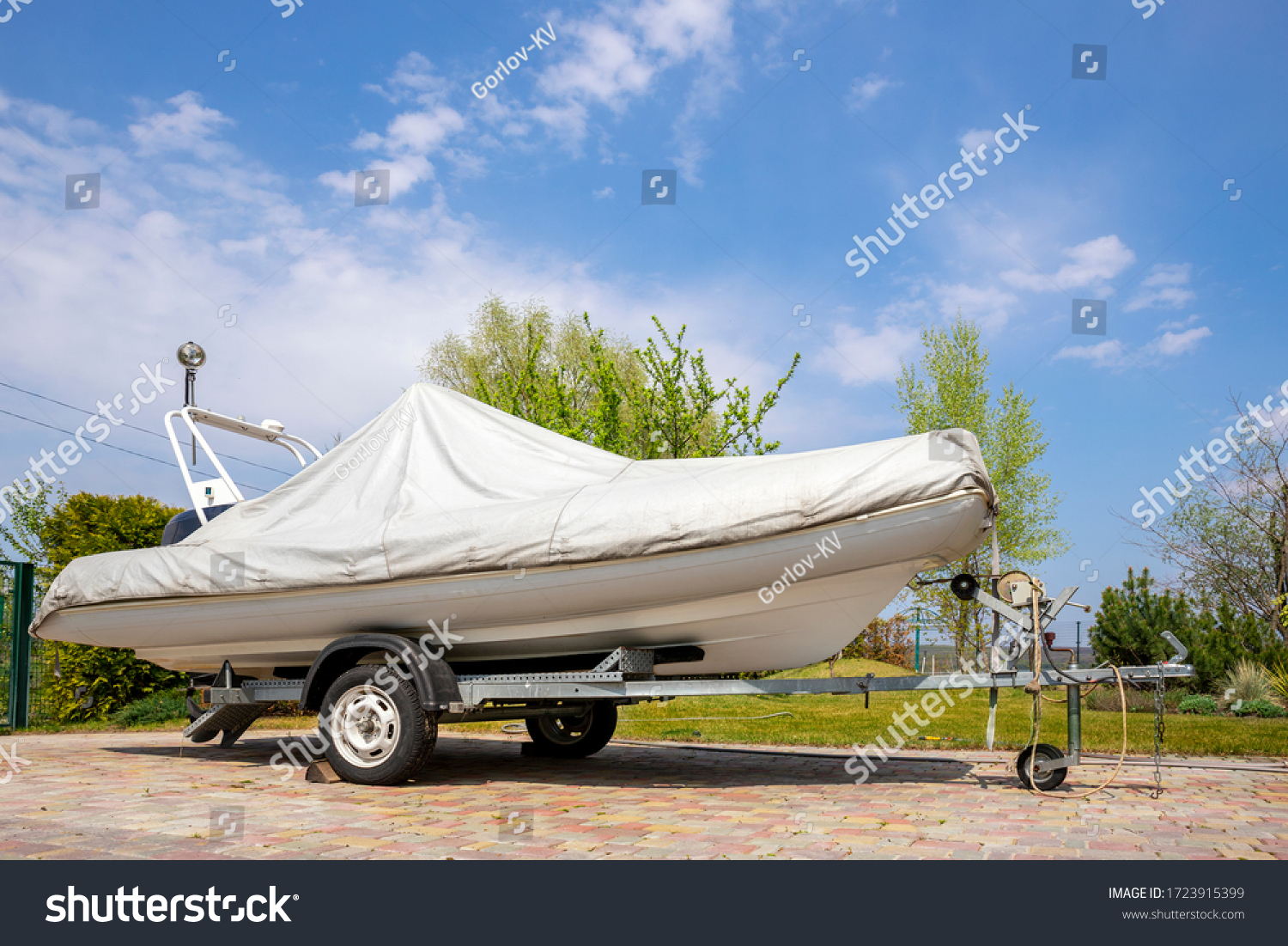 Big modern inflatable motorboat ship covered with grey or white protection tarp standing on steel semi trailer at home backyard on bright sunny day with blue sky on background. Boat vessel storage #1723915399