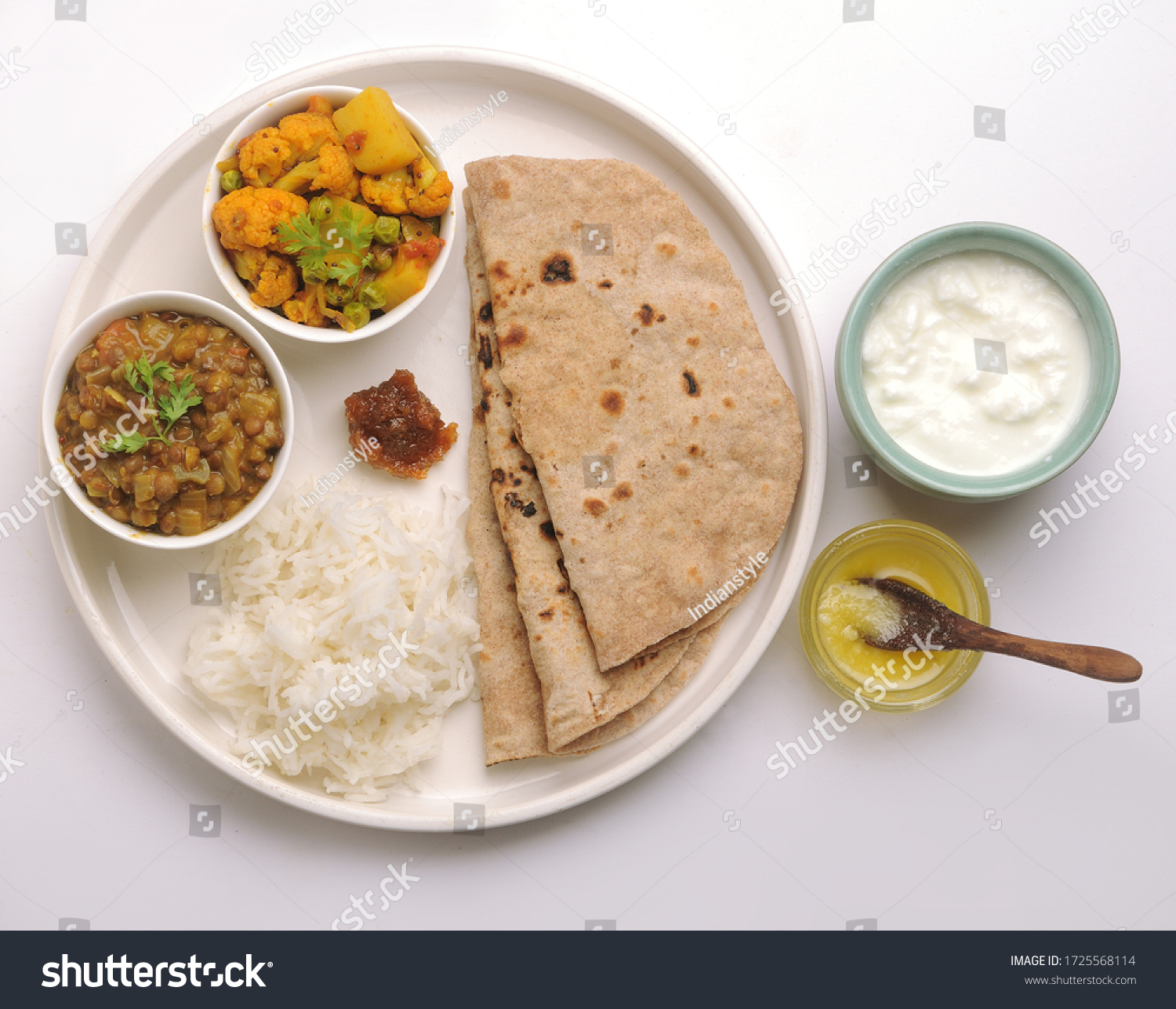 vegetarian Indian thali or Indian home food with lentil dal, cauliflower curry, roti or Indian flat bread, ghee butter, lemon pickle, rice, curd or yogurt #1725568114