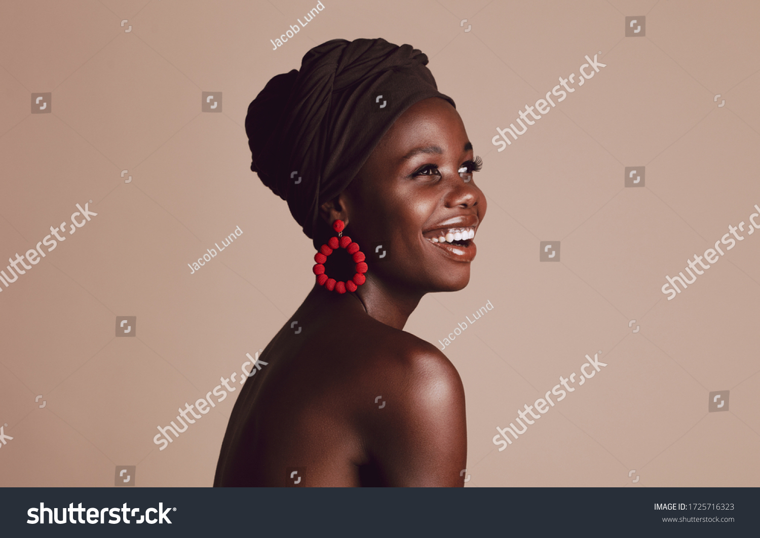 Close up of smiling african woman on beige background. Beautiful female model with a cloth wrapped on head looking away and smiling. #1725716323