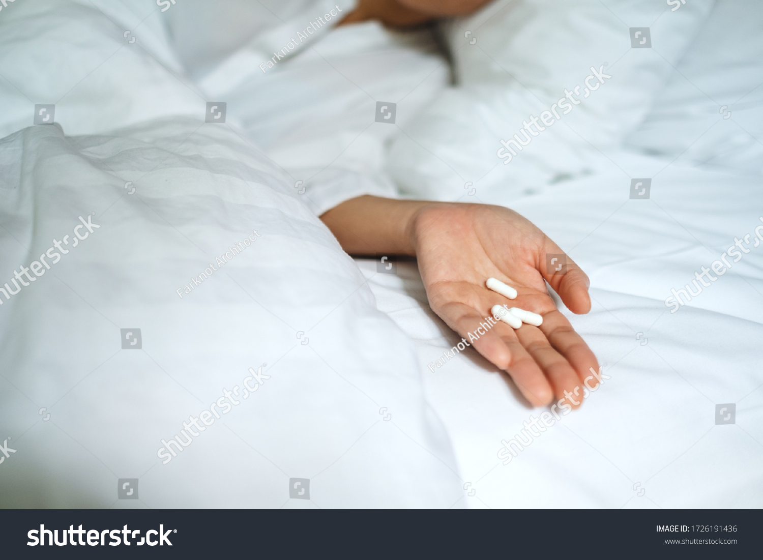 Closeup image of a sick woman sleeping and lying down on a bed with white pills in hand #1726191436