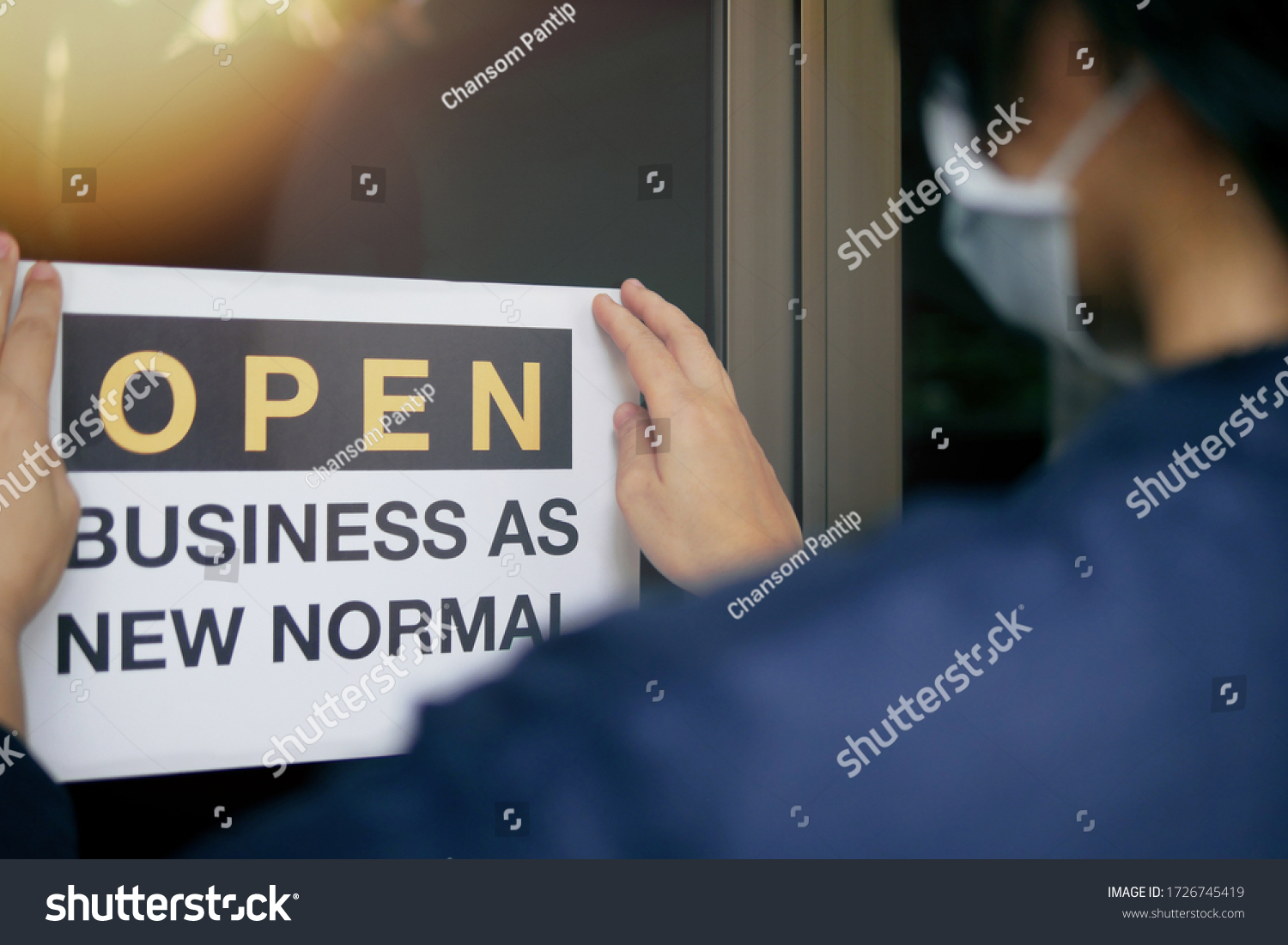 Reopening for business adapt to new normal in the novel Coronavirus COVID-19 pandemic. Rear view of business owner wearing medical mask placing open sign “OPEN BUSINESS AS NEW NORMAL” on front door. #1726745419