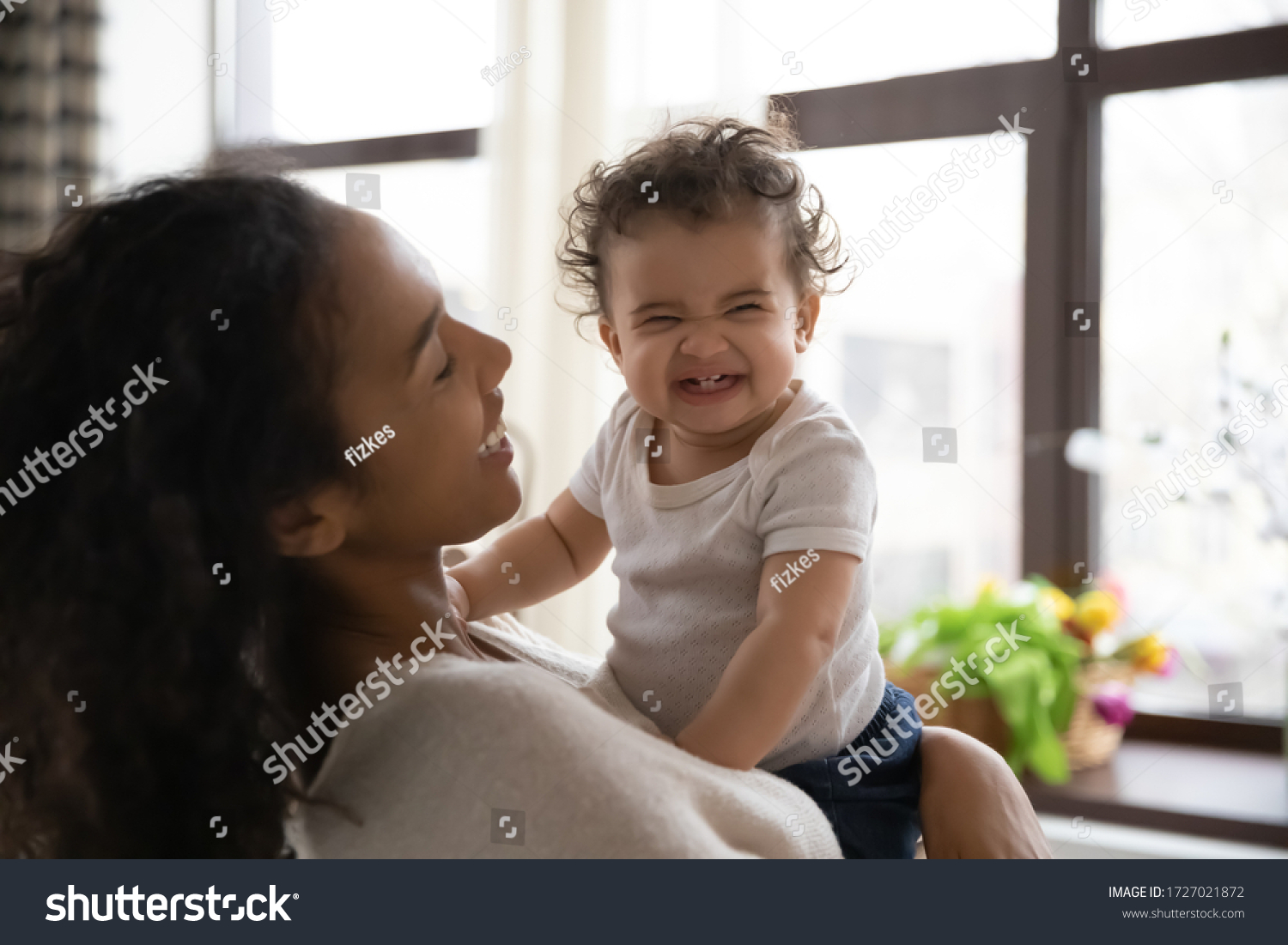 Loving young african American mother hold in arms cute funny infant toddler showing first teeth, caring happy biracial mom hug embrace smiling little baby girl child, motherhood, childcare concept #1727021872