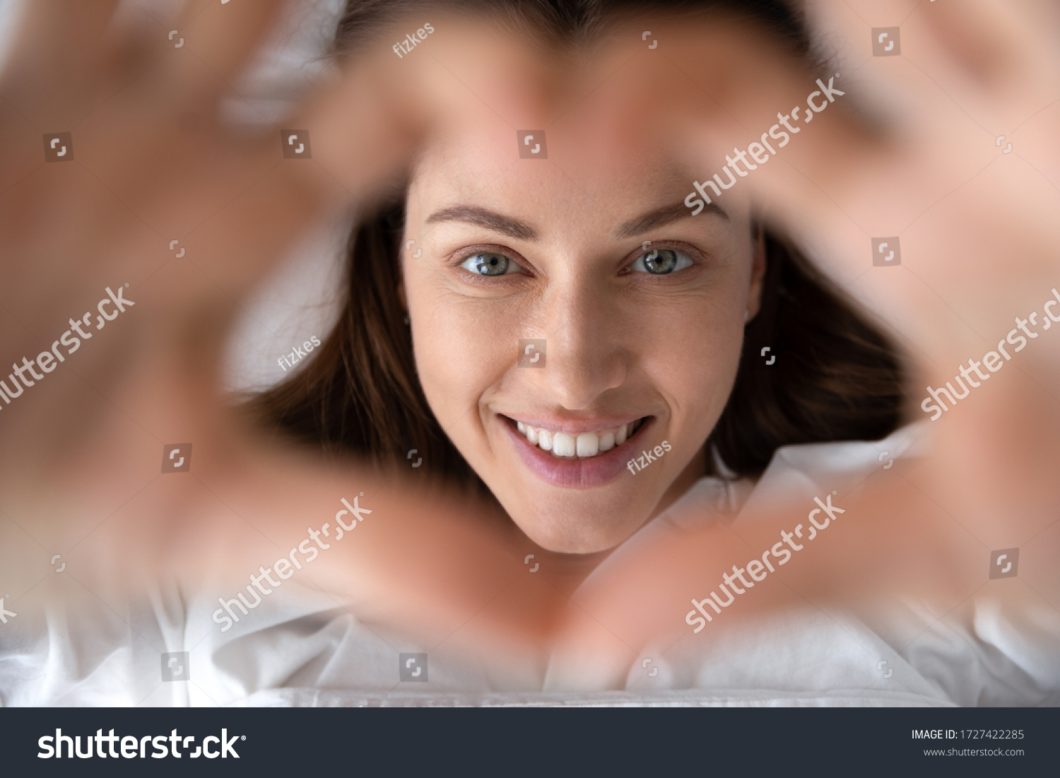 Woman in love wakeup lies in bed look at camera showing with hands heart shape close up view from above focus on happy face, mattress pillow high quality bedclothes, good morning enjoy new day concept #1727422285