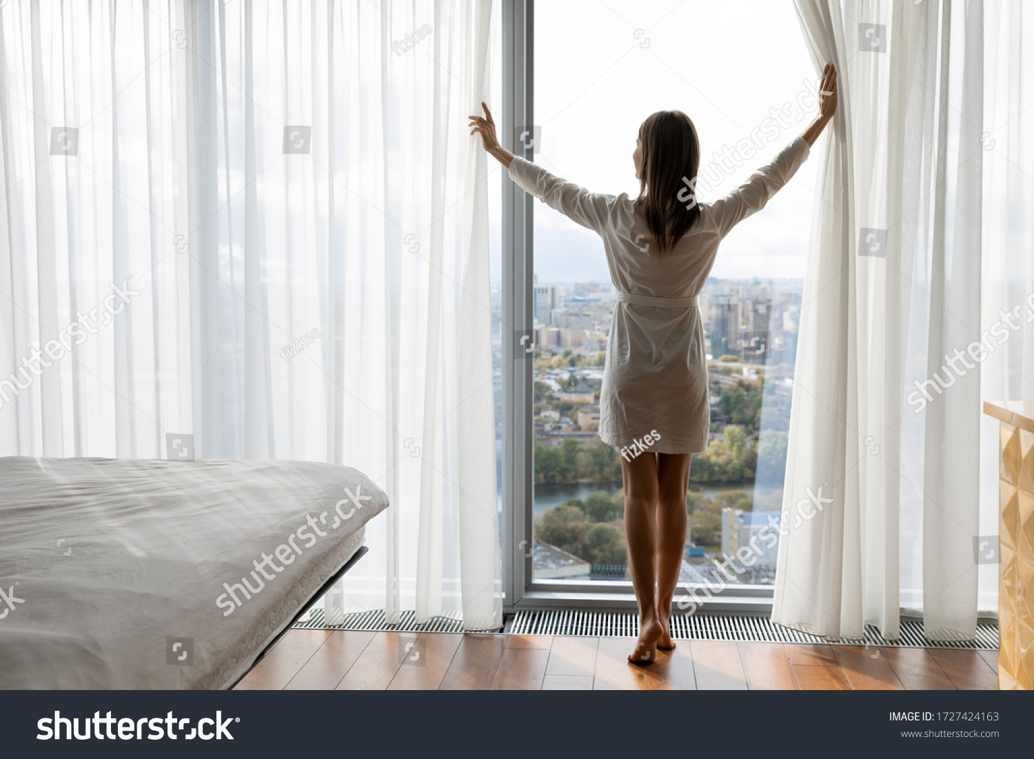 Rear full length of woman opened curtains enjoys big picturesque city standing barefoot on warm heated floor near panoramic window enjoy urban view, climate control at home, welcoming new day concept #1727424163