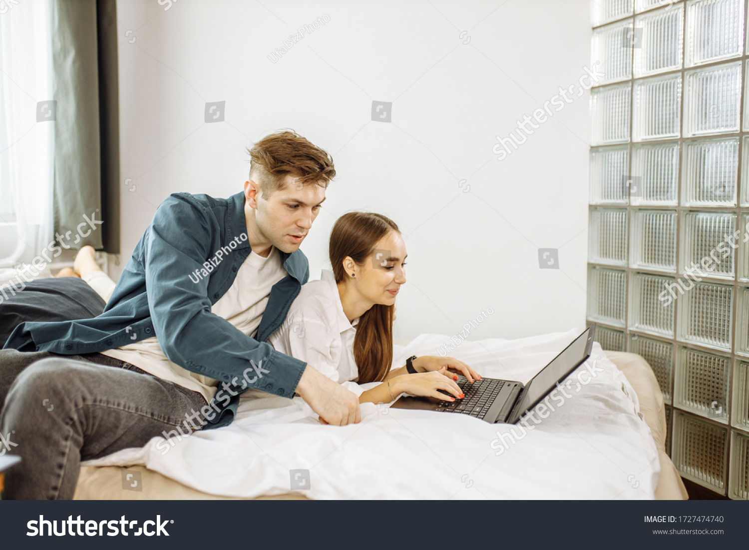 free time of beautiful young caucasian couple at home, man and woman have a rest together, use laptop lying on bed. during quarantine, weekends. spare time #1727474740