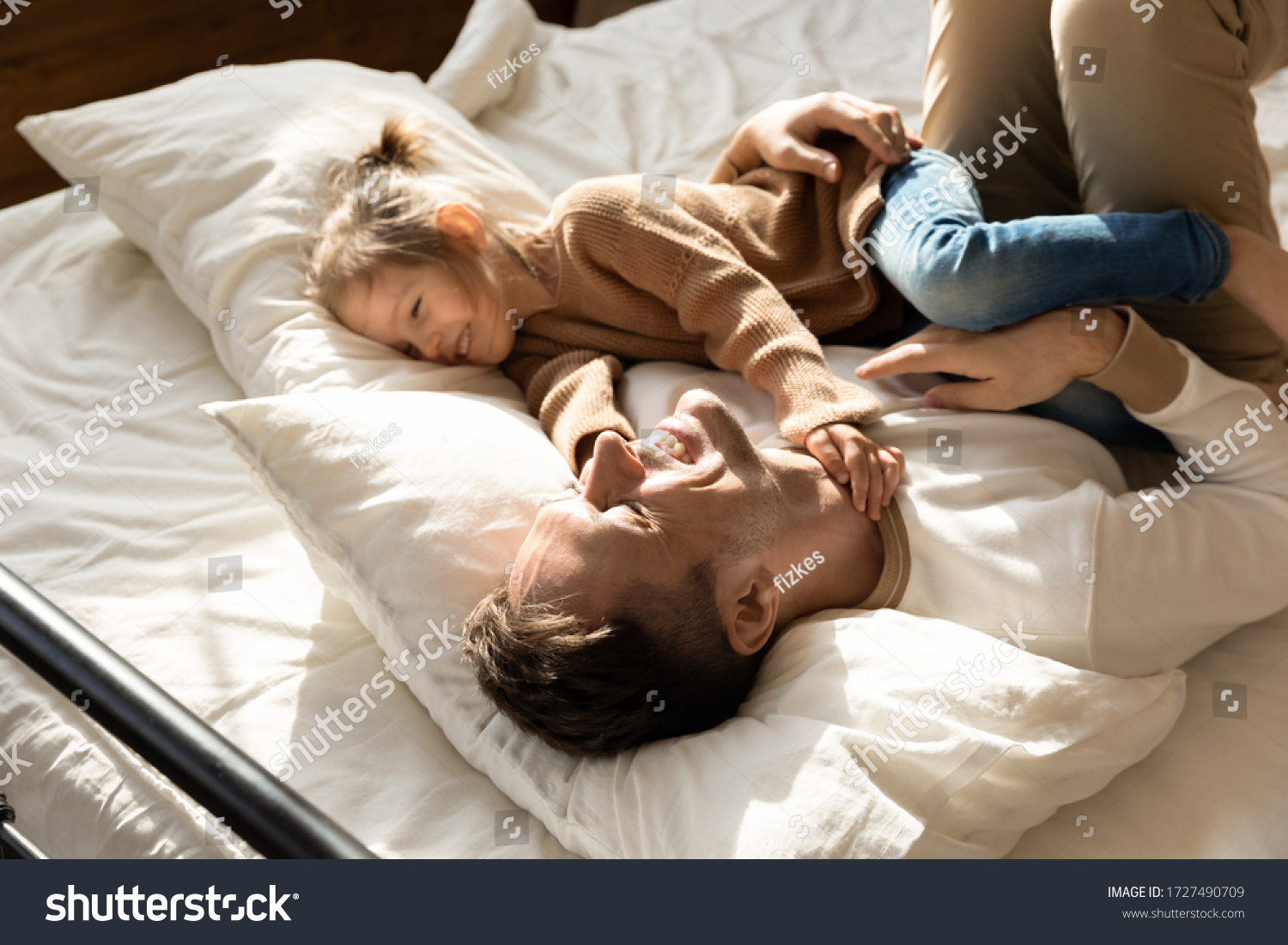 Happy father and little daughter relaxing in cozy bed together, smiling dad having fun with cute preschool girl, resting, taking nap in bedroom, family spending weekend together, enjoying free time #1727490709