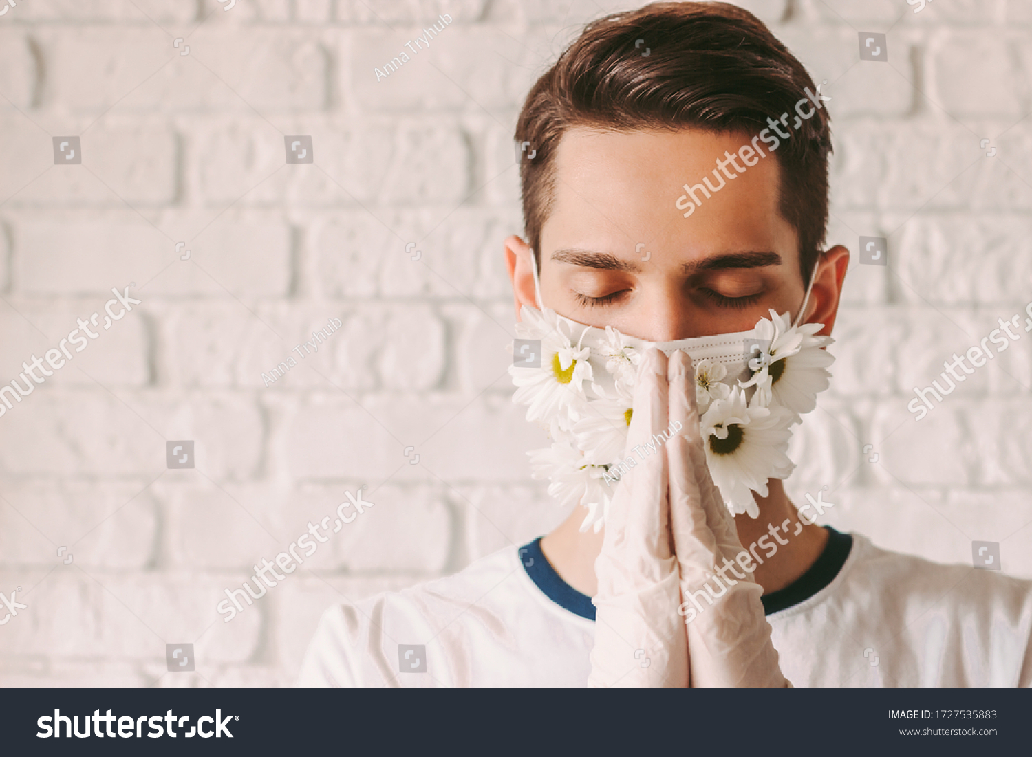 Portrait faithful young man in medical face mask with flowers praying to God for help with coronavirus COVID-19. Religious male doctor in protective gloves and summer face mask with praying hands #1727535883