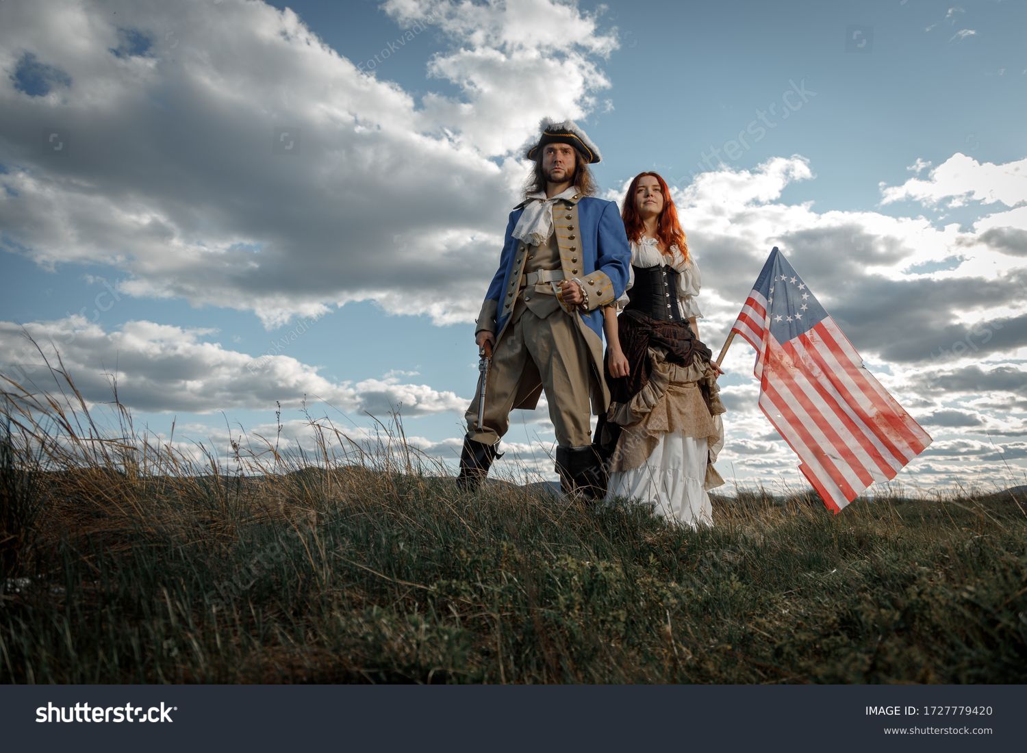 Man in form of officer of War of Independence and girl in historical dress of 18th century. July 4 is US Independence Day. Couple of patriots freedom fighters in outdoor on background cloudy sky #1727779420