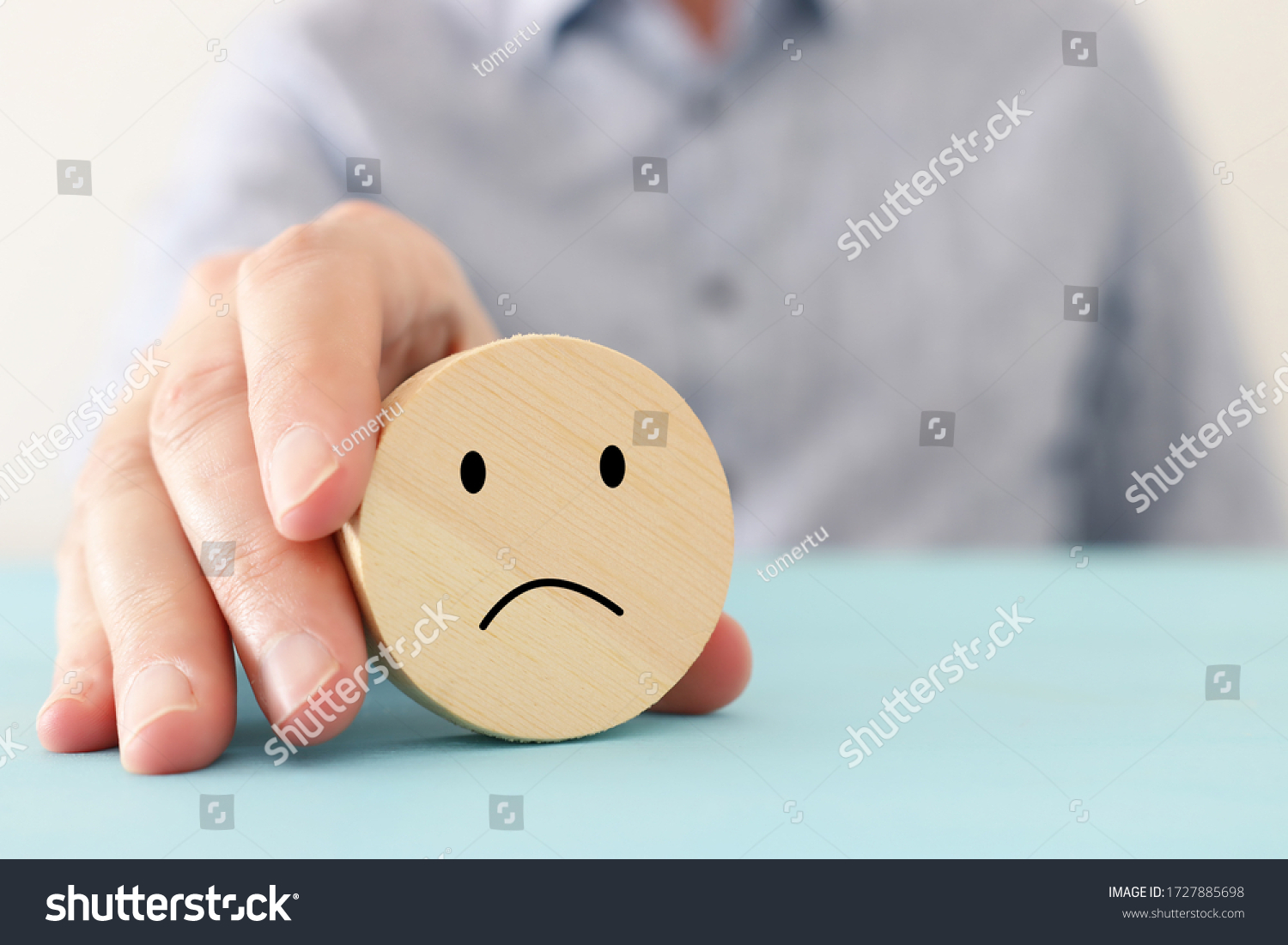 male hand holding wooden cube with sad face. concept of anxiety, stress or sad emotions #1727885698