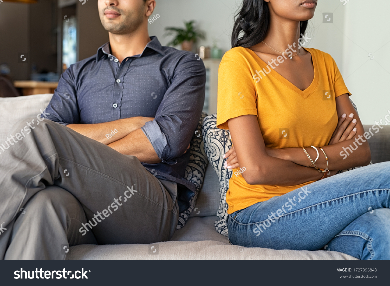 Middle eastern couple sitting back to back after a fight. Young indian couple in fight with arms crossed sitting on couch after quarrel at home. Young mixed race woman and his boyfriend sitting angry. #1727996848