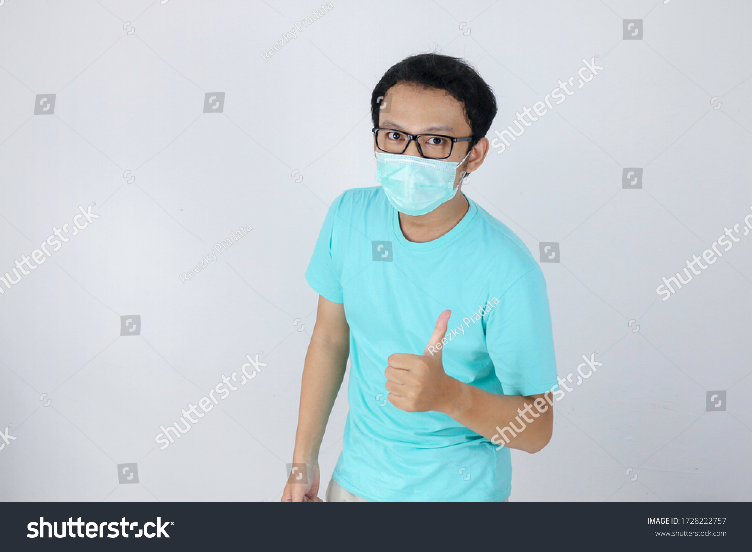 Young Asian Man wear medical mask is give ok hand sign with confident gestures. Indonesian man wearing blue shirt. #1728222757