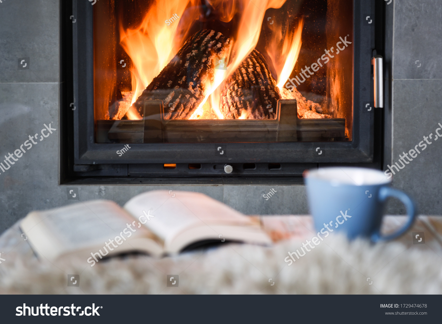 Open book, cup of tea and warm plaid near burning fireplace. Hygge concept #1729474678