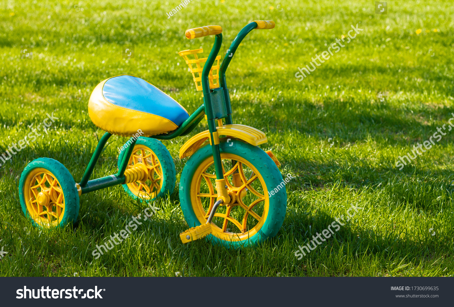 Small yellow and green children's tricycle standing on the grass on a sunny day. Copy space