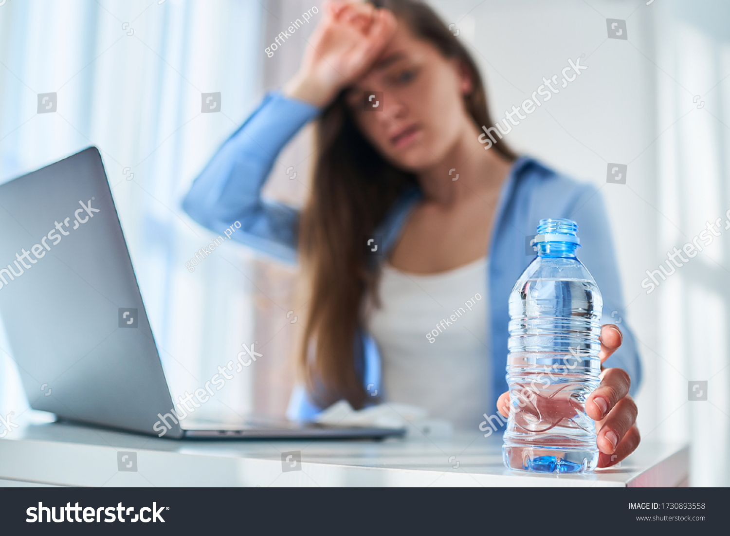 Upset tired working woman suffering from heat, thirst and hot weather cools down with cold water bottle during online work at computer at warm summer day #1730893558